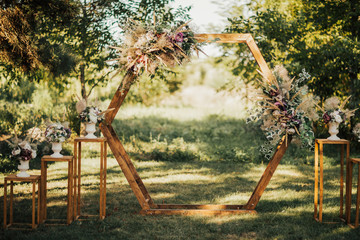 Wedding wooden arch in rustic style decorated with grass hay field color and flowers. Near wooden...