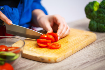 Closeup of woman slices tomato for diet salad
