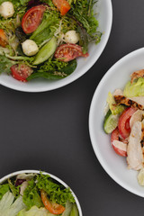 white deep plates with fresh salad ingredients mixed with sauce placed on an gray background. A place for a menu, banner or advertisement
