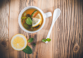 Mint tea leaves in a cup with fresh slice lemon on wooden table.