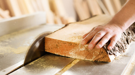 Worker hands details of wood cutter machine with a circular saw and wooden board. Circular cutting...