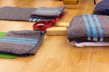 Grey blankets with blue strips and other yoga props widespread over studio wooden planks floor. Belts, blocks and colorful mats in wellness centre. Class, lesson concepts