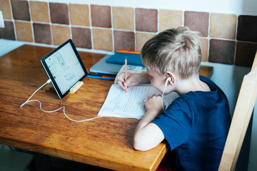 Online learning. A schoolboy learns from a textbook and digital tablet online. Remote schooling staying at home. Quarantine and social isolation for safety in an epidemic. Family education. Homework