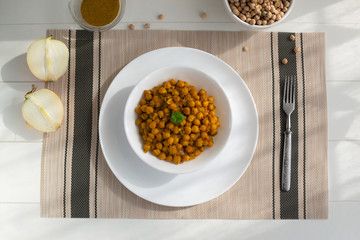 Braised chickpeas with onions and curry in a white plate on a light background. Vegetarian food. Healthy eating