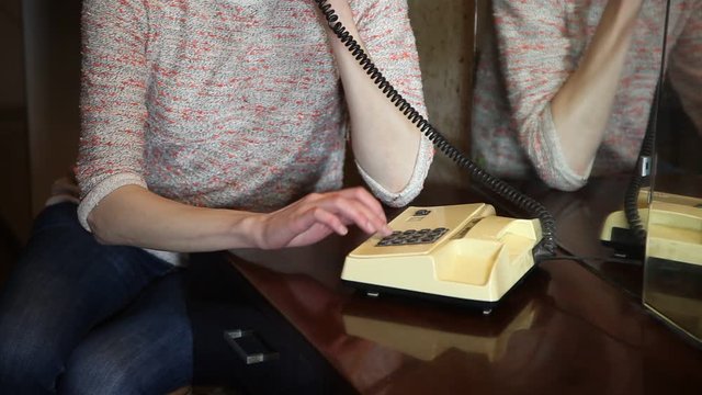 Woman is speaking on retro soviet phone, sitting near mirror. Reflection of woman.   Old soviet flat ret