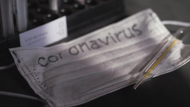 Coronavirus. Medical test tubes are in the organizer. Medical disposable gauze bandages are on the table. A mercury glass thermometer rests on a protective medical mask.