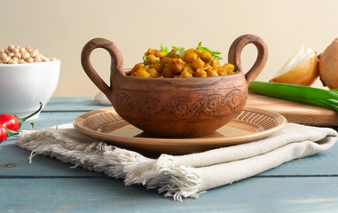 Braised chickpeas with onions and curry in a ceramic bowl on a wooden background. Rustic style. Vegetarian food. Healthy eating