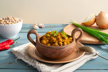 Braised chickpeas with onions and curry in a ceramic bowl on a wooden background. Rustic style. Vegetarian food. Healthy eating