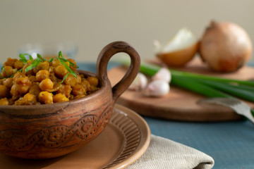 Braised chickpeas with onions and curry in a ceramic bowl on a wooden background. Rustic style. Vegetarian food. Healthy eating