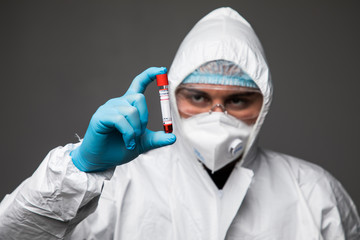 Coronavirus pandemia. The epidemic of the Chinese coronavirus virologist man in a protective suit, gloves, mask and glases examines the virus in a tube isolated on gray background