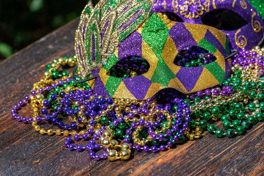 Mardi Gras Color Beads With Masks On Wooden Table In Sunlight