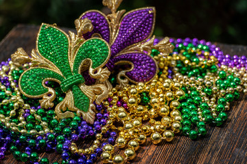 Mardi Gras color beads with fleur de lis on wooden table in sunlight © Lynne Ann Mitchell