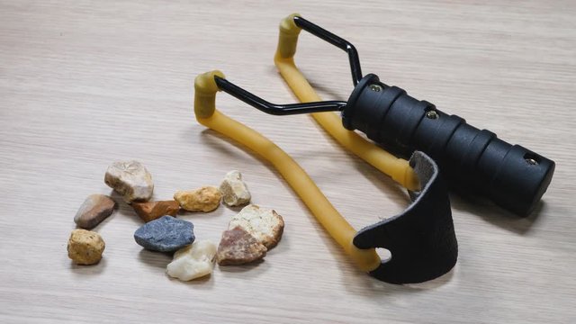 Slingshot small hand-powered projectile weapon. Classic form Y-shaped frame held in off hand with two rubber strips attached to uprights. Other ends of strips lead back to pocket that holds projectile