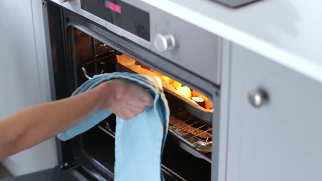 Woman Roasting Tray Of Vegetables For Vegan Meal In Oven