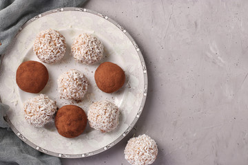 Energy balls of nuts and oatmeals with coconut flakes and cocoa on white plate on gray background, horizontal format