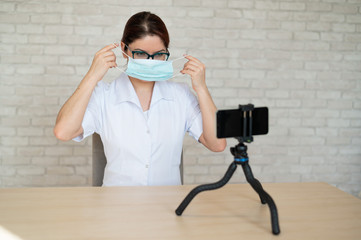 Remote appointment with a physician in quarantine. A doctor shows how to wear a medical mask for...