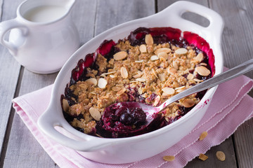 Berry crumble in white baking dish on white wooden background.