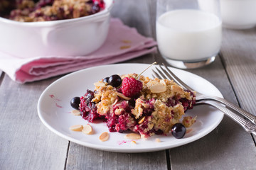 Berry crumble in white plate on grey wooden background.