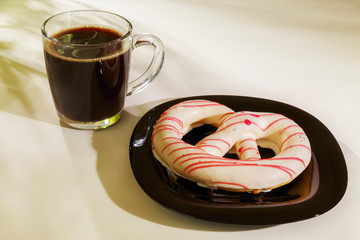 The pretzel cake is on a plate on the table. There is a Cup of coffee next to it. The photo of the Breakfast was taken in the morning light.