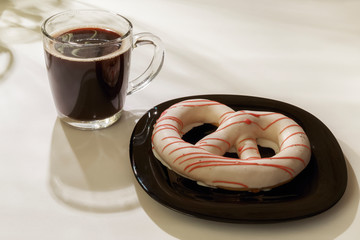 The pretzel cake is on a plate on the table. There is a Cup of coffee next to it. The photo of the Breakfast was taken in the morning light.