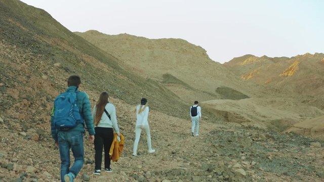 Group of tourist walk along the rock canyon in hot desert, tourists take picture and have fun. Desert mountains background, Egypt, Sinai, slow motion, 4k