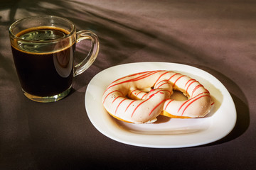 The pretzel cake is on a plate on the table. There is a Cup of coffee next to it. The photo of the Breakfast was taken in the morning light.