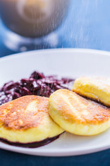 Breakfast and delicious concept - Pancakes from cottage cheese with jam, blue background. Sprinkle with icing sugar.