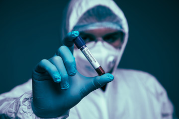 Man laboratory technician wear in protective clothes hold on blood sample tube for corona virus test. COVID 19 test