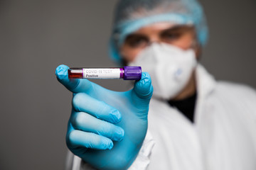 Virologist in a medical mask and protective clothing holds a test tube with positive blood sample for coronavirus testing. Pandemic covid19. Respiratory syndrome, panic, experiences, research