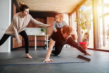 Father entertaining his baby while doing single arm plank at home