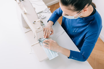 Girl sews masks to protect against the corona virus. Woman hands using the sewing machine to sew the face medical mask during the pandemia.