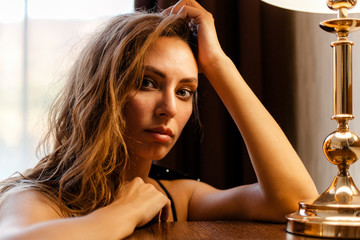 Close up portrait of a mysterious Caucasian woman leaning on a table next to a lamp. The concept of...
