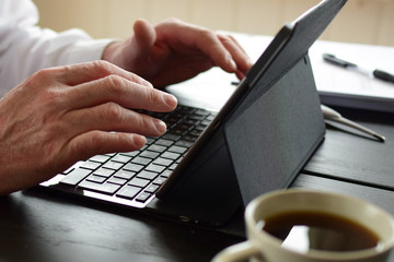 Freelancer man sits at a table and takes notes in a laptop. Concept: freelancer at home behind a laptop screen, remote work in quarantine. Hands and laptop closeup.