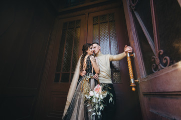 Beautiful bride and groom with a wreath of flowers are hugging in a vintage interior near a wooden...