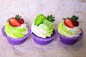 Three cupcakes with whipped cream, chocolate bar, strawberry ,decorated macaroons on crumpled paper. Picture for a menu or a confectionery catalog. with space for text.