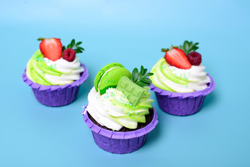 Three cupcakes with whipped cream, chocolate bar, strawberry ,decorated macaroons on blue background. Picture for a menu or a confectionery catalog. with space for text.
