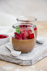 Italian dessert - chocolate panna cotta, mousse, cream or pudding with cherry sauce in a glass jar on a board on a light concrete background. Vertical orientation. Copy space