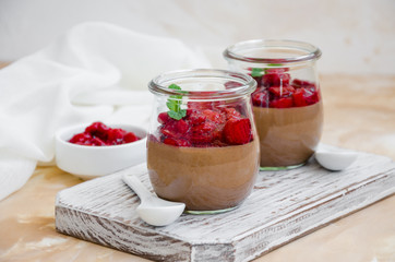 Italian dessert - chocolate panna cotta, mousse, cream or pudding with cherry sauce in a glass jar on a board on a light concrete background. Horizontal orientation. Copy space