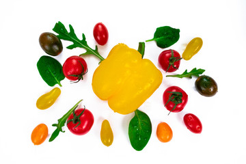 Cherry tomatoes of different colors, arugula leaves and basil around a bell yellow pepper. Fresh vegetables and herbs isolated on white