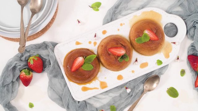 Caramel custard puddings on white ceramic tray and kitchen countertop.