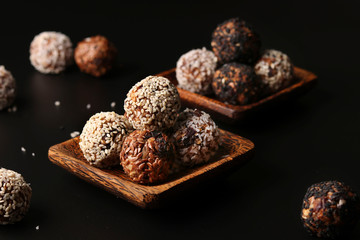 Healthy energy balls of nuts, oatmeals and dried fruit with coconut, flax and sesame seeds on wooden coconut plates on a black background, horizontal orientation