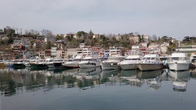 clear sunny warm day. Private yachts and sailing boats with lowered sails standing on pier in bay. Reflections in water. People walk along promenade. Turkey, Istanbul, Tarabya, February 2020.