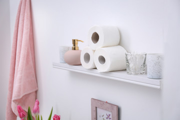 Toilet paper rolls, soap dispenser and cotton swabs on shelf in bathroom