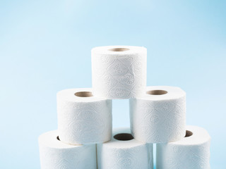 Stack of white toilet paper rolls on blue abstract background. Personal hygiene supplies for restroom. Panic concept during coronavirus pandemic.