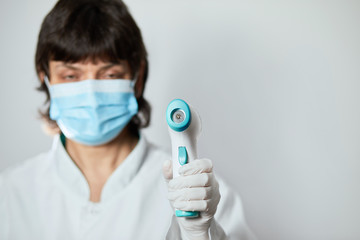 Doctor wearing protective  mask ready to use infrared forehead thermometer  to check body temperature for virus symptoms - epidemic virus outbreak concept. Coronavirus.Thermometer gun