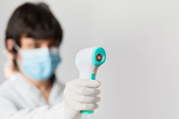 Doctor wearing protective  mask ready to use infrared forehead thermometer  to check body...
