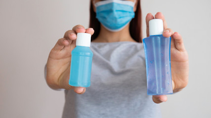 A woman with a surgical mask holding two plastic bottles of alcohol gel in both hands.