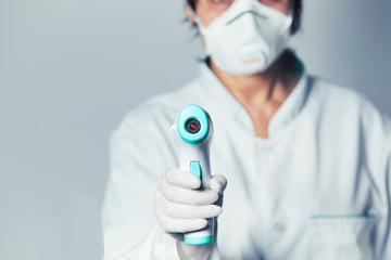Doctor wearing protective  mask ready to use infrared forehead thermometer  to check body...