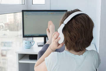 Fototapeta premium girl with headphones, view from the back sitting in front of a computer, put her legs on the table, relaxed posture, working from home, freelance, self-isolation, preventing measures from coronavirus