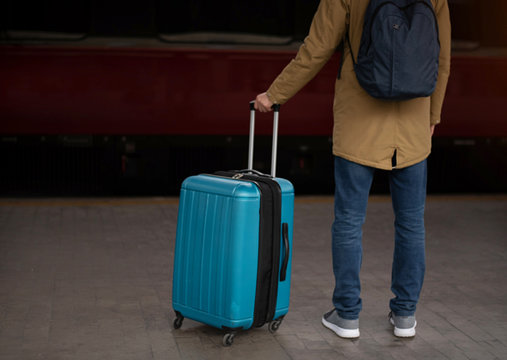 A young man with a blue suitcase is waiting for the train. Train station.